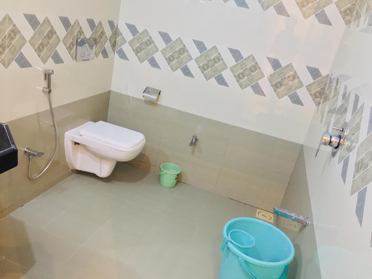 A bathroom with a toilet, a shower, and a bucket.