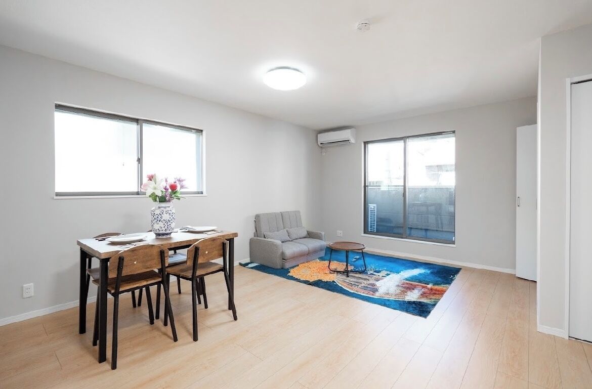 A spacious living room with a dining area, large windows, and a colorful rug.