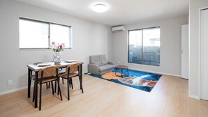 A spacious living room with a dining area, large windows, and a modern air conditioning unit. - Seiran Villa (Osaka)