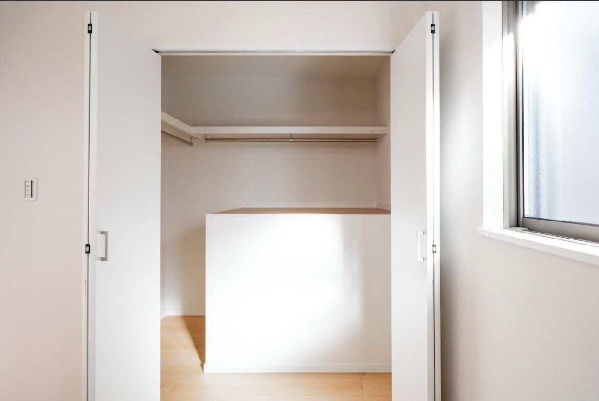 A room with a large white wardrobe, a wooden floor, and a window on the right side.