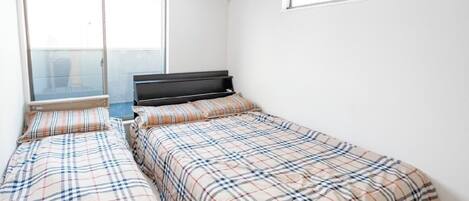 A bedroom with two beds, a window, and an air conditioning unit.