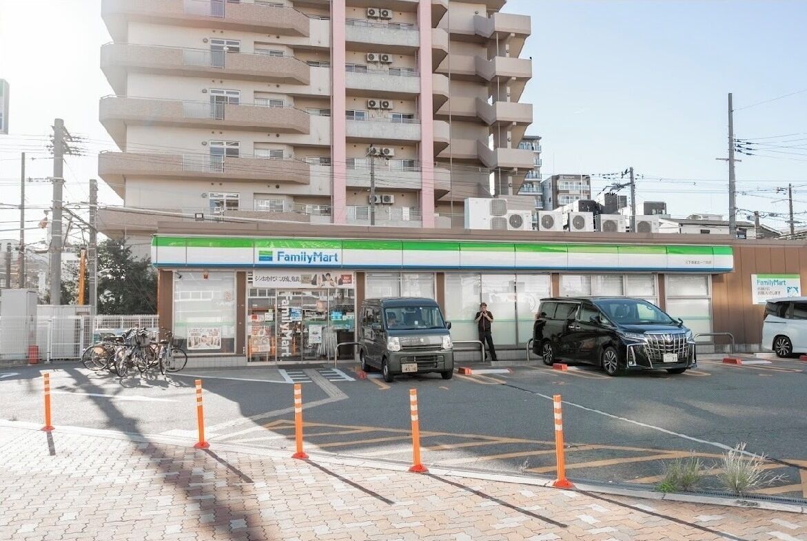 Una tienda FamilyMart con estacionamiento, un aparcamiento para bicicletas y un edificio de varios pisos al fondo.