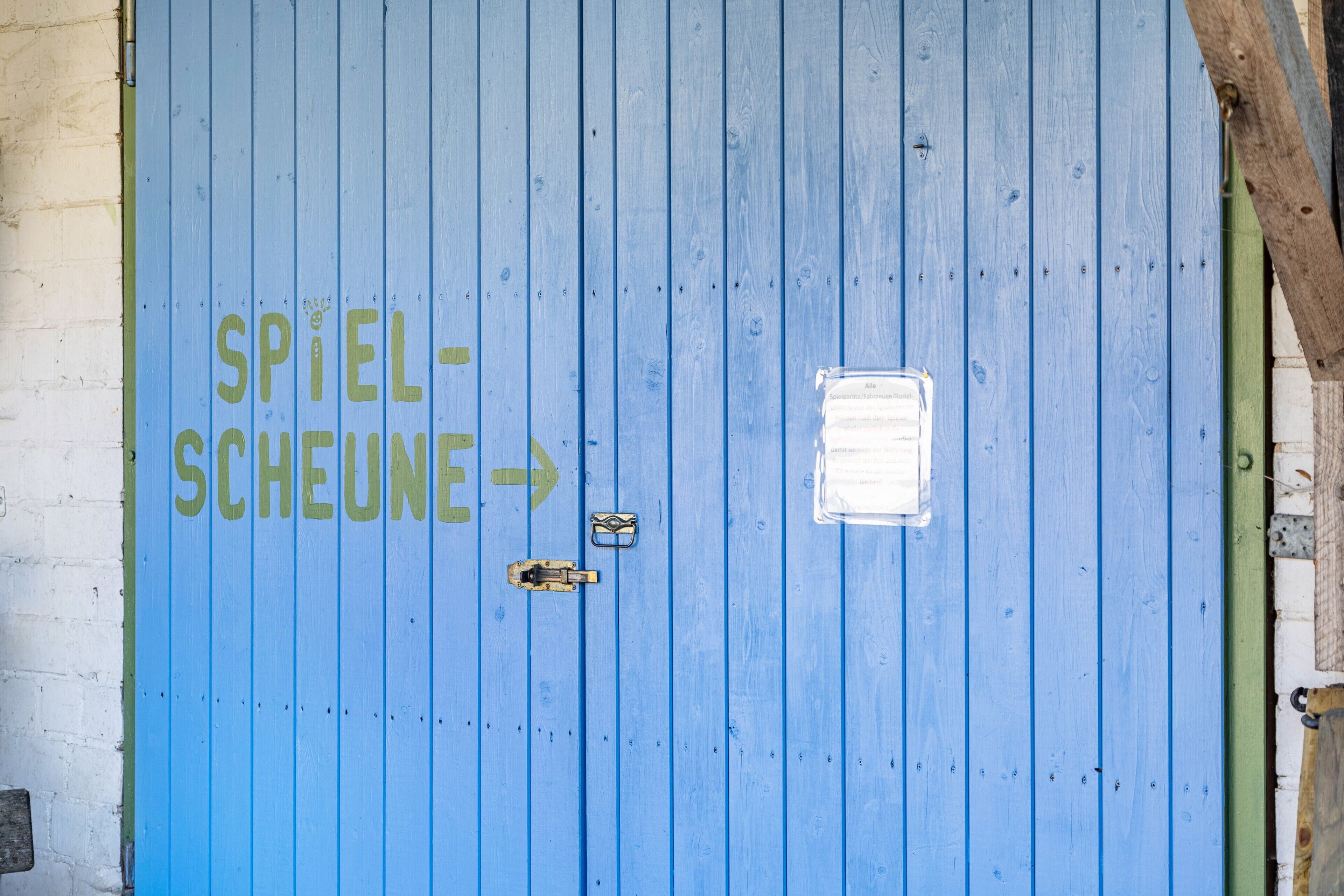 A blue door with the text 'SPIEL-SCHEUNE' and an arrow pointing to the right.