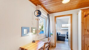Une pièce avec un plafond en bois, une fenêtre avec des rideaux, une table avec des chaises et une vue sur une autre pièce où se trouve un canapé.