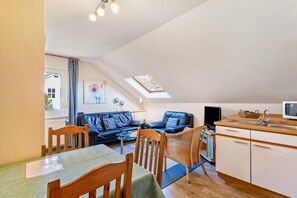 A cozy living room with a sofa, a dining table, and a kitchen area with a sink and microwave. - Apartment "Erle" with Shared Garden and Wi-Fi (Olsberg)
