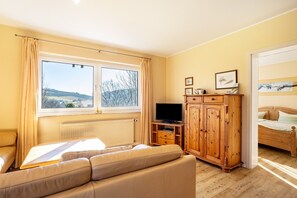 Een slaapkamer met een bed, een televisie, een houten kledingkast en een raam met gordijnen.