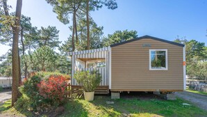 A small, single-story mobile home with a sloped roof, a window, and a door. It is surrounded by trees and has a small porch area. - Amorosa Mobile Home, Bonne Anse Plage at La Palmyre (La Palmyre)