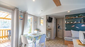 A dining area with a table and chairs, a television, and a sofa with shelves. - Amorosa Mobile Home, Bonne Anse Plage at La Palmyre (La Palmyre)