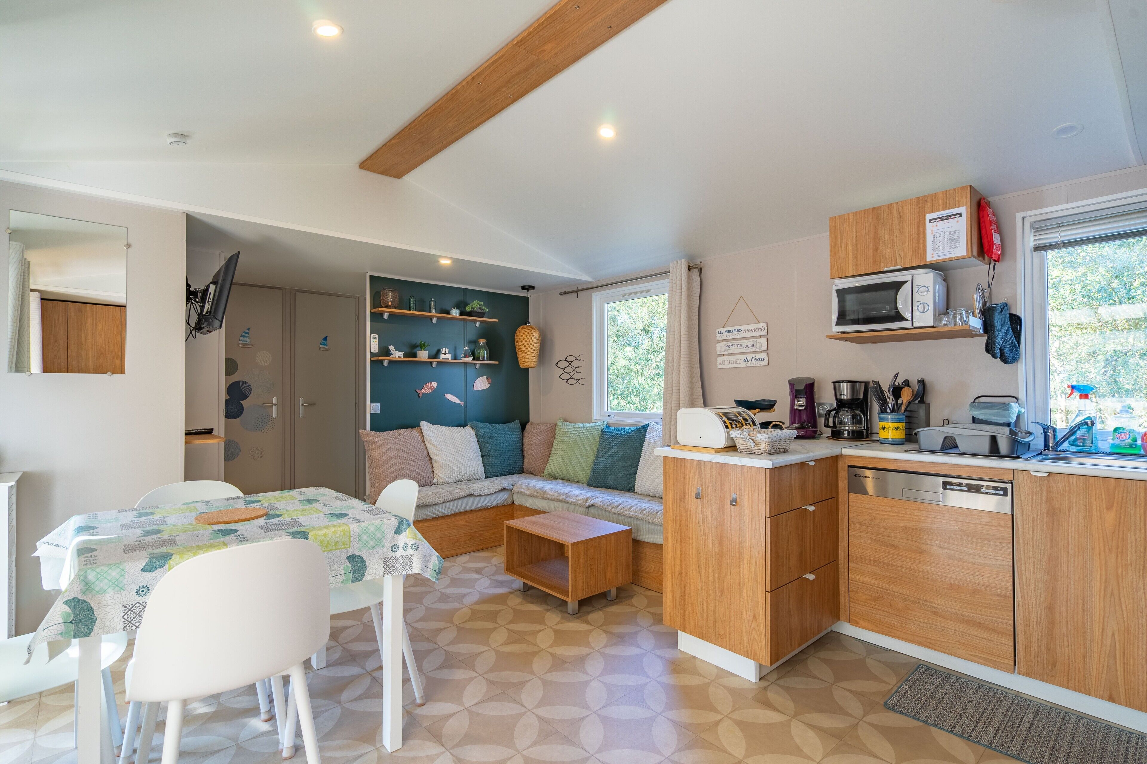Cocina compacta con microondas, cafetera y lavabo. Hay un comedor con mesa y sillas, y una sala de estar con sofá.
