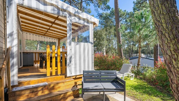 A wooden deck with a bench, a covered outdoor area, and a view of a forested area. - Amorosa Mobile Home, Bonne Anse Plage at La Palmyre (La Palmyre)