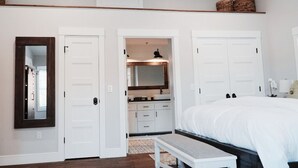 Un dormitorio con una cama grande, un banco, un espejo y un baño con lavabo y espejo.