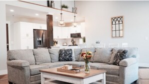 Una sala de estar moderna con un sofá seccional gris, una mesa de centro de madera y una cocina al fondo.