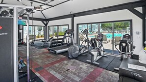 Un gimnasio con equipo de ejercicio, una cinta de correr y vistas a una piscina.