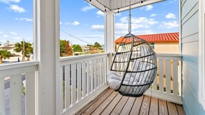 Eine Veranda mit einer Hängematte, weißen Geländern und Blick auf ein Gebäude mit rotem Dach.