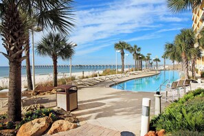 A pool area with lounge chairs, palm trees, and a view of the beach and pier. - ☀️Stunning Beach Front-Tiki Bar-Pools-Calypso 1-706☀️ (Panama City Beach)