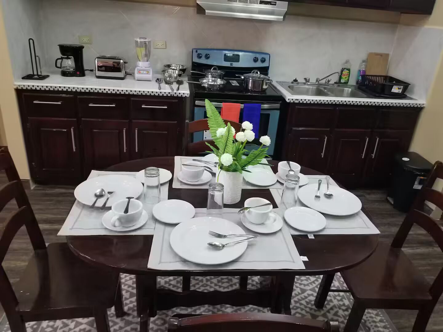 Un coin repas avec une table dressée pour quatre personnes, une cuisinière et un évier en arrière-plan.