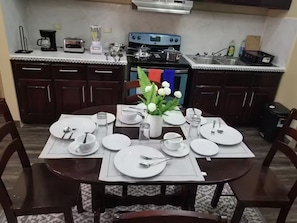 Een eetgedeelte met een tafel voor vier personen, een kookplaat en een spoelbak op de achtergrond.