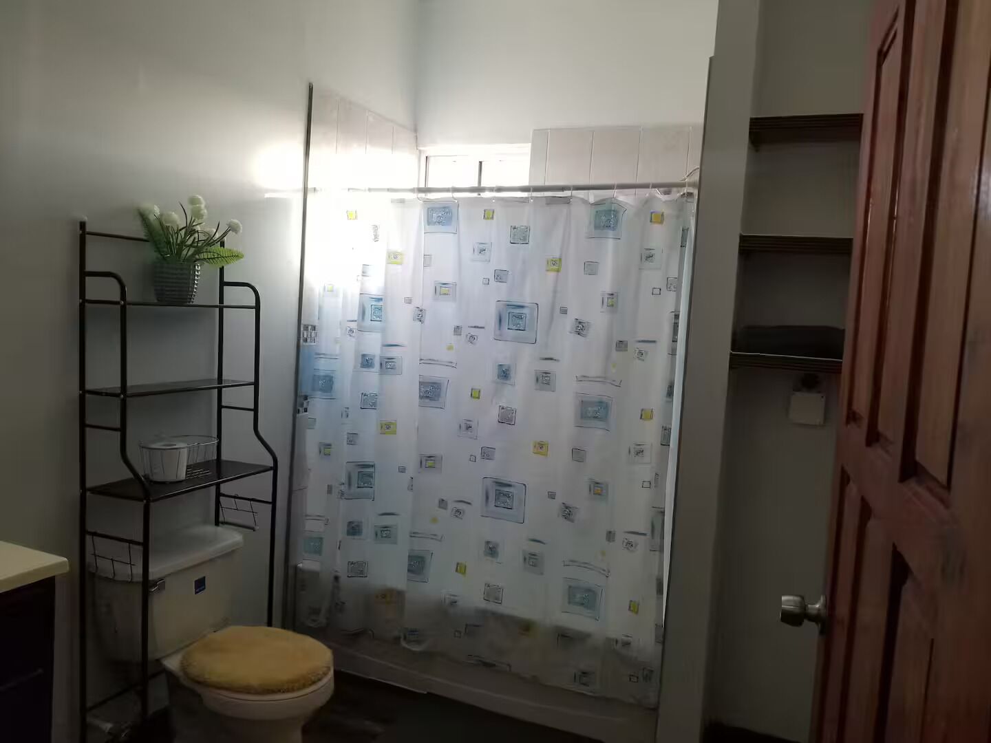 Un baño pequeño con inodoro, cortina de ducha y repisa metálica con una planta.