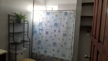 Un baño pequeño con inodoro, cortina de ducha y repisa metálica con una planta.