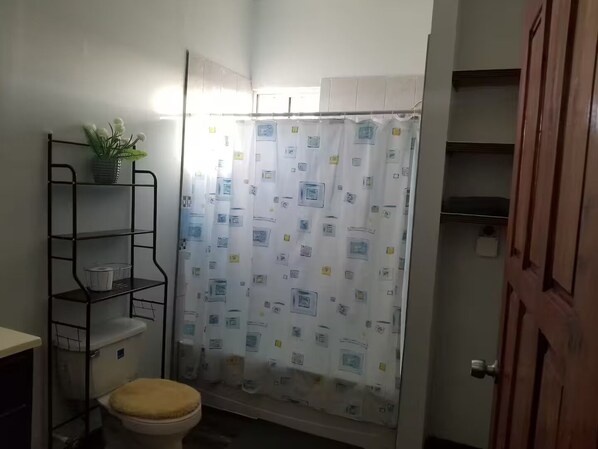 A small bathroom with a toilet, a shower curtain, and a metal shelf with a plant.