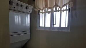 Un espace buanderie équipé d’un lave-linge et d’un sèche-linge, une fenêtre avec des rideaux et un four fixé au mur.