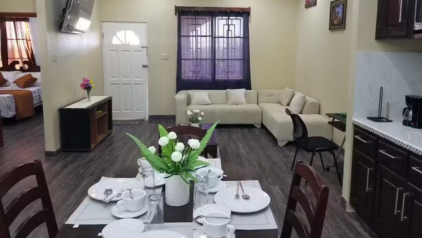 Un comedor con una mesa preparada para cuatro personas, un sofá y una zona de cocina.