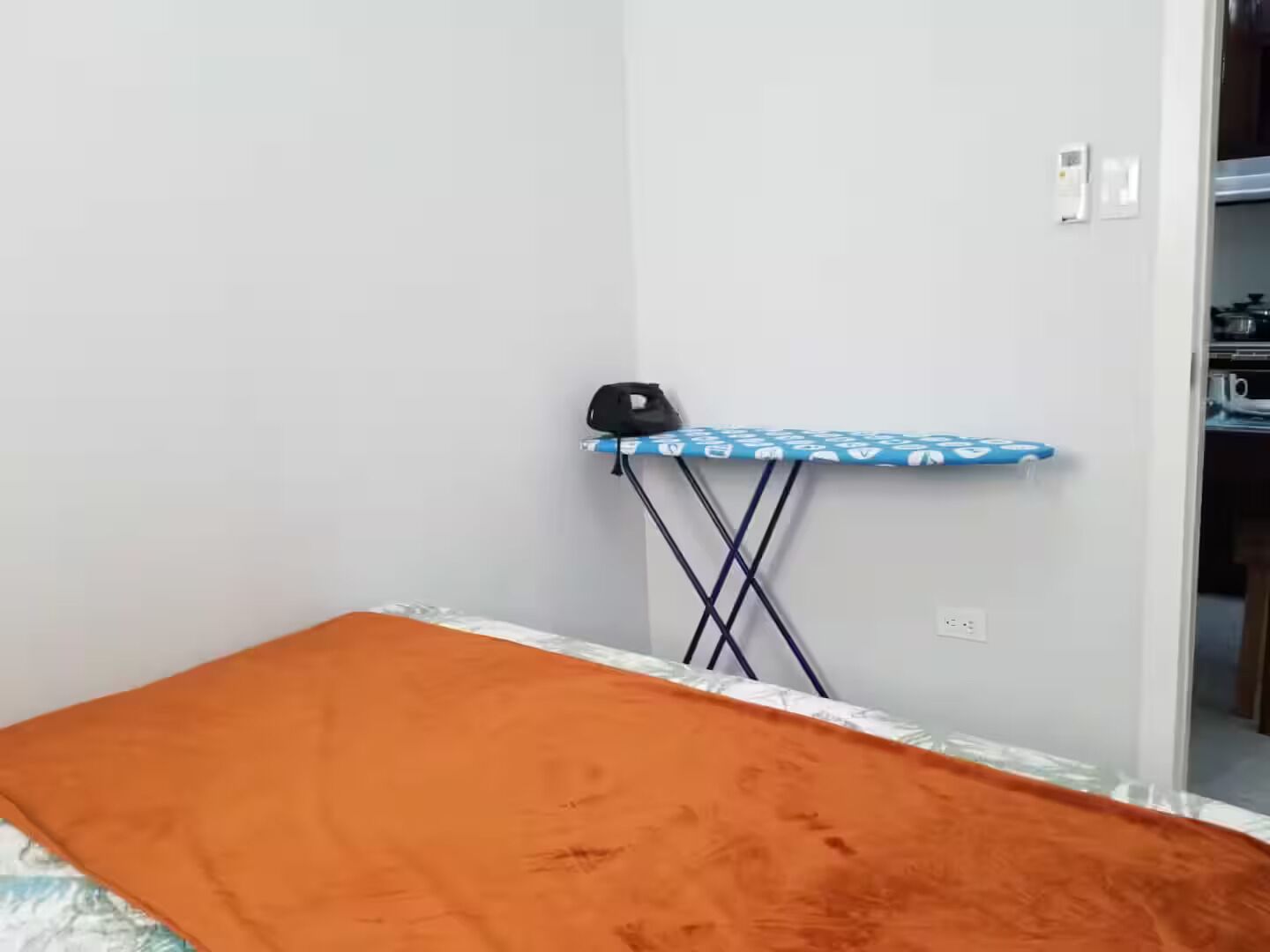 Una habitación con cama, tabla de planchar y armario.