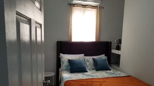 Een slaapkamer met een bed, een nachtkastje, een raam met gordijnen en een radiator.