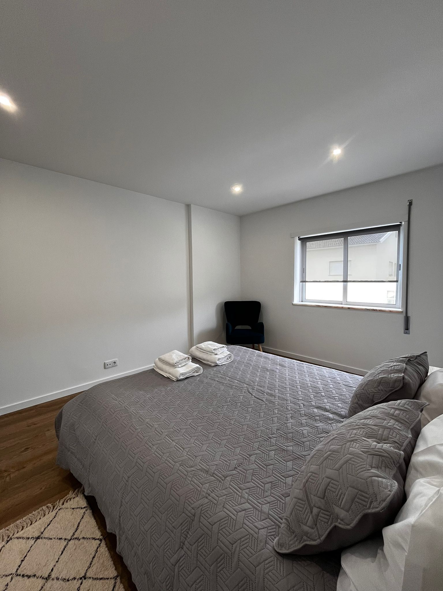A modern bedroom with a large bed, a window, and a chair.