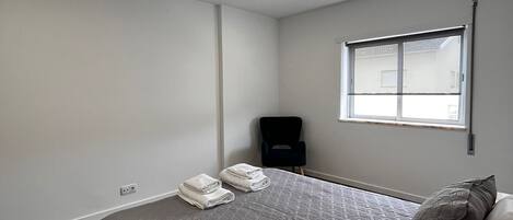 A modern bedroom with a large bed, a window, and a chair.