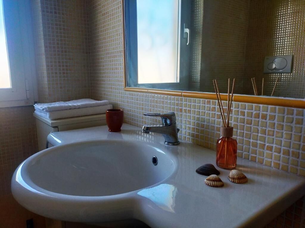 Een badkamer met een witte wastafel, een spiegel en een raam.