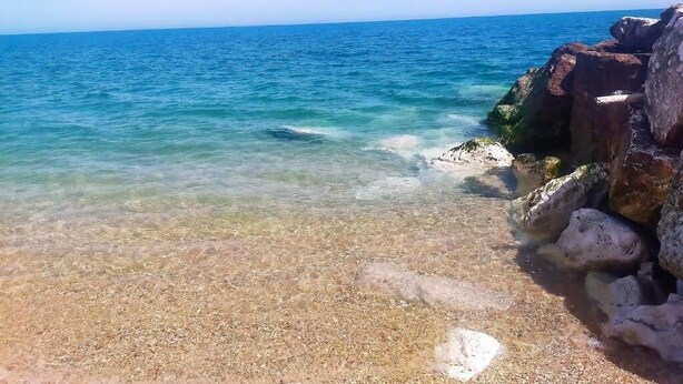 Ein klarer Strand mit ruhigem Wasser und Felsformationen.