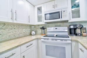 A modern kitchen with white cabinets, a microwave, a stove, a blender, and a coffee maker. - Strollin' to Mad Beach Condo (Madeira Beach)