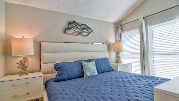 Un dormitorio con una cama grande, dos mesitas de noche, una lámpara de pared y una ventana con persianas.