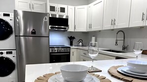 A modern kitchen with stainless steel appliances, white cabinetry, and a central island with a glass of water and a bowl. - Casitas at Coconut Grove (Miami)