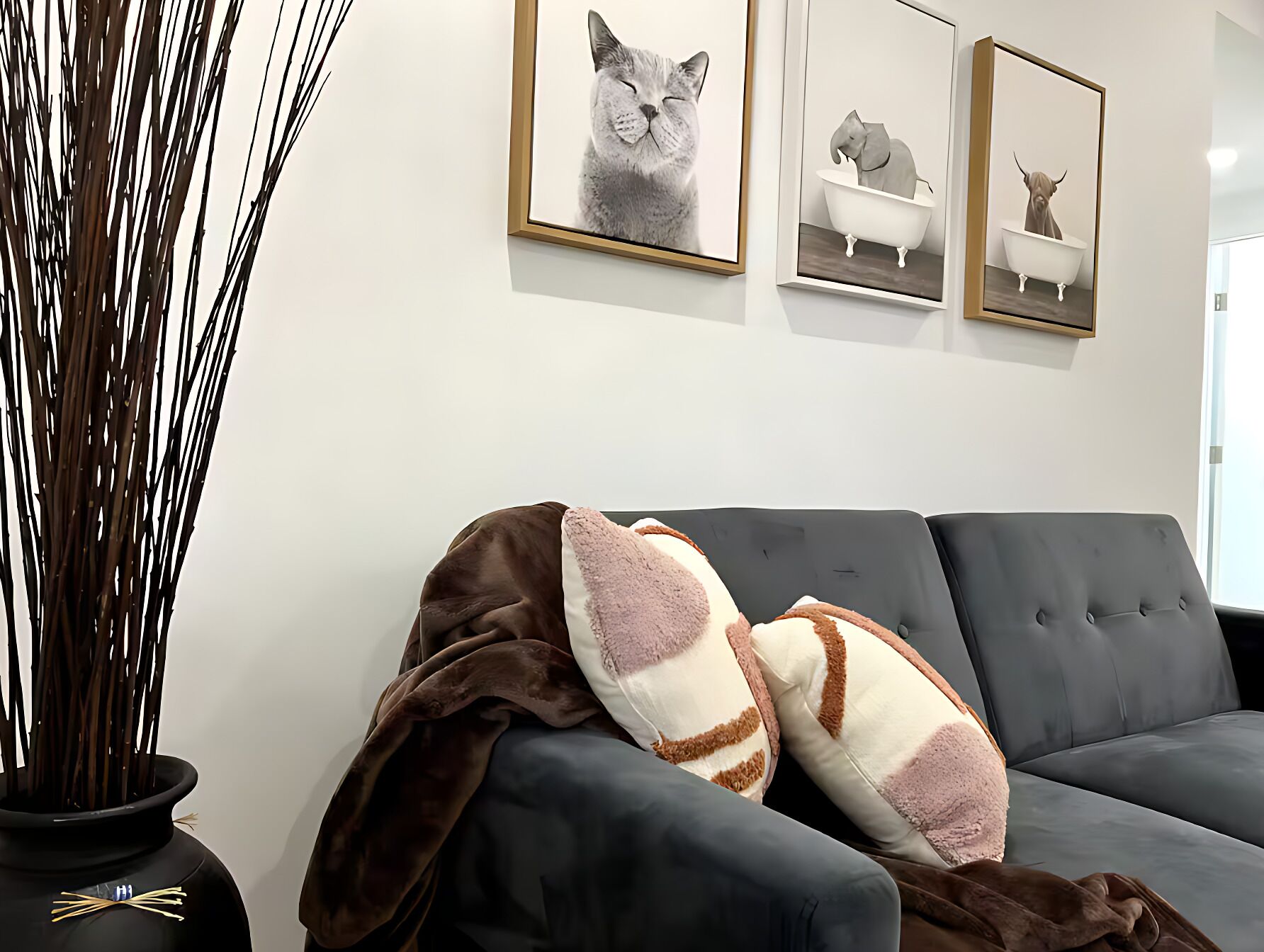 Ein Wohnzimmer mit einem grauen Sofa, einer Vase mit Ästen und drei gerahmten Bildern an der Wand.