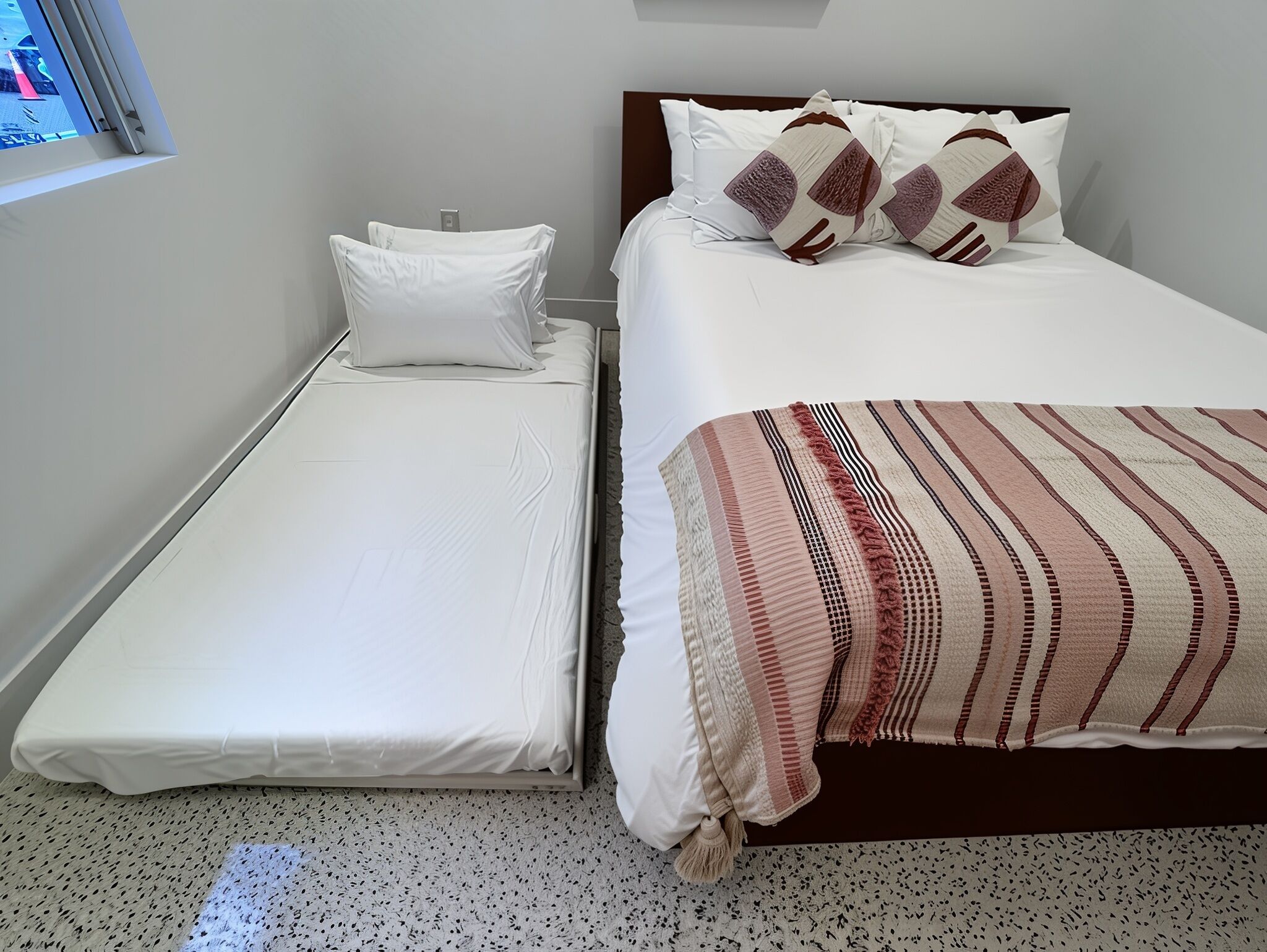 Una camera piccola con un letto singolo, una finestra, una coperta a righe e una TV a muro.