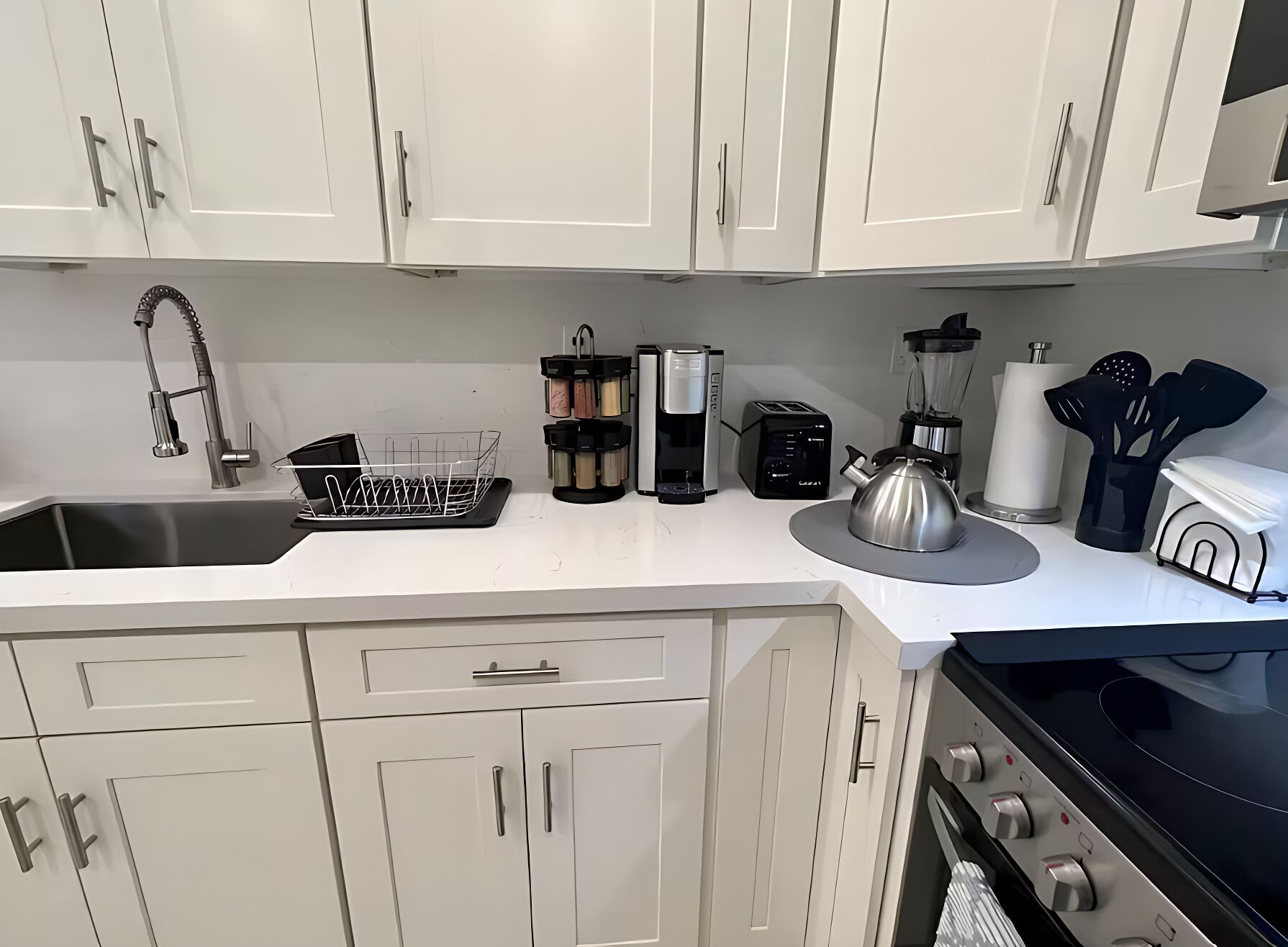 Una cocina moderna con armarios blancos, un lavamanos de acero inoxidable, un hervidor, una cafetera y un tostador.