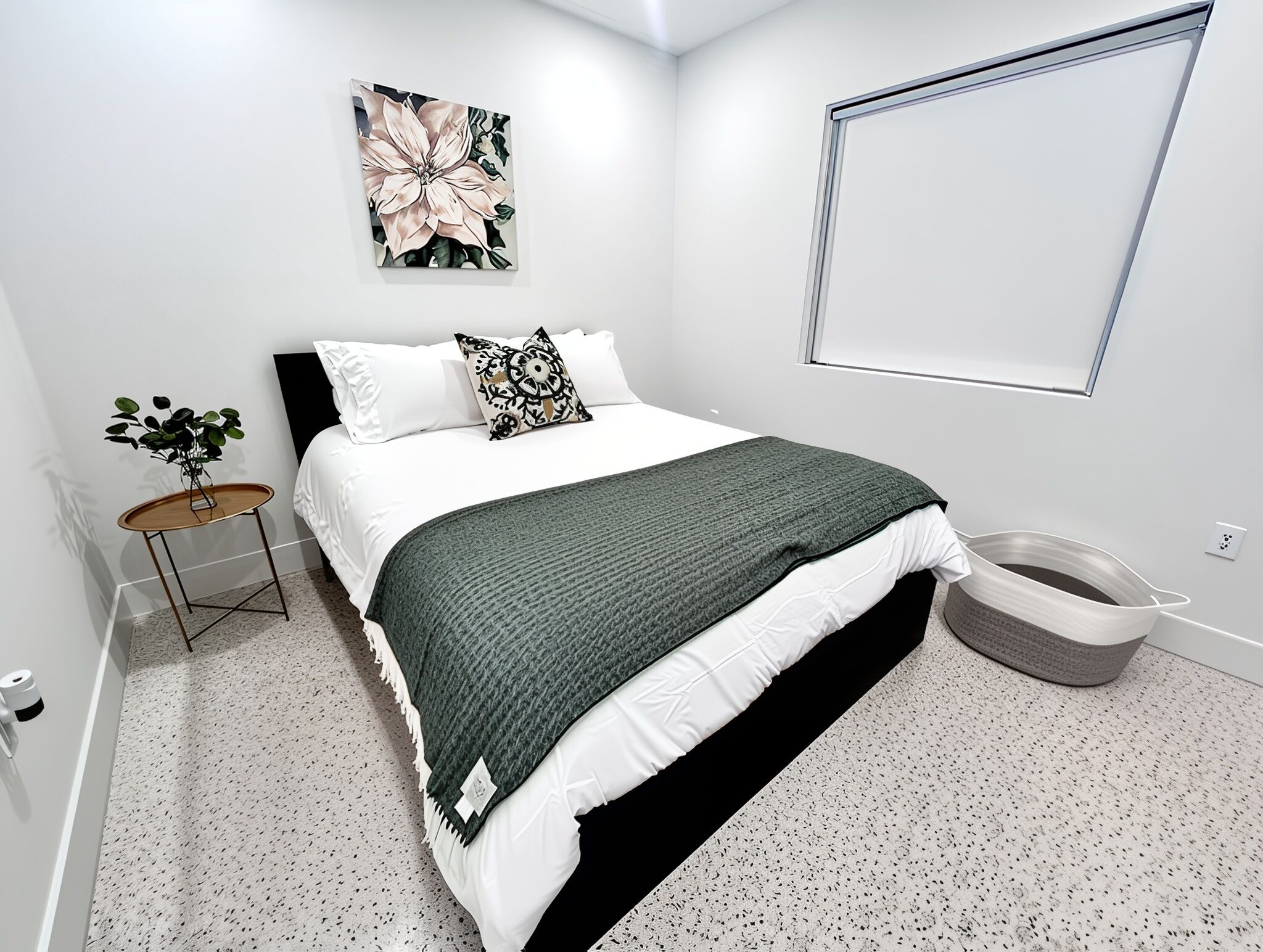 Quarto moderno com cama, mesa de cabeceira, planta e uma obra de arte na parede.