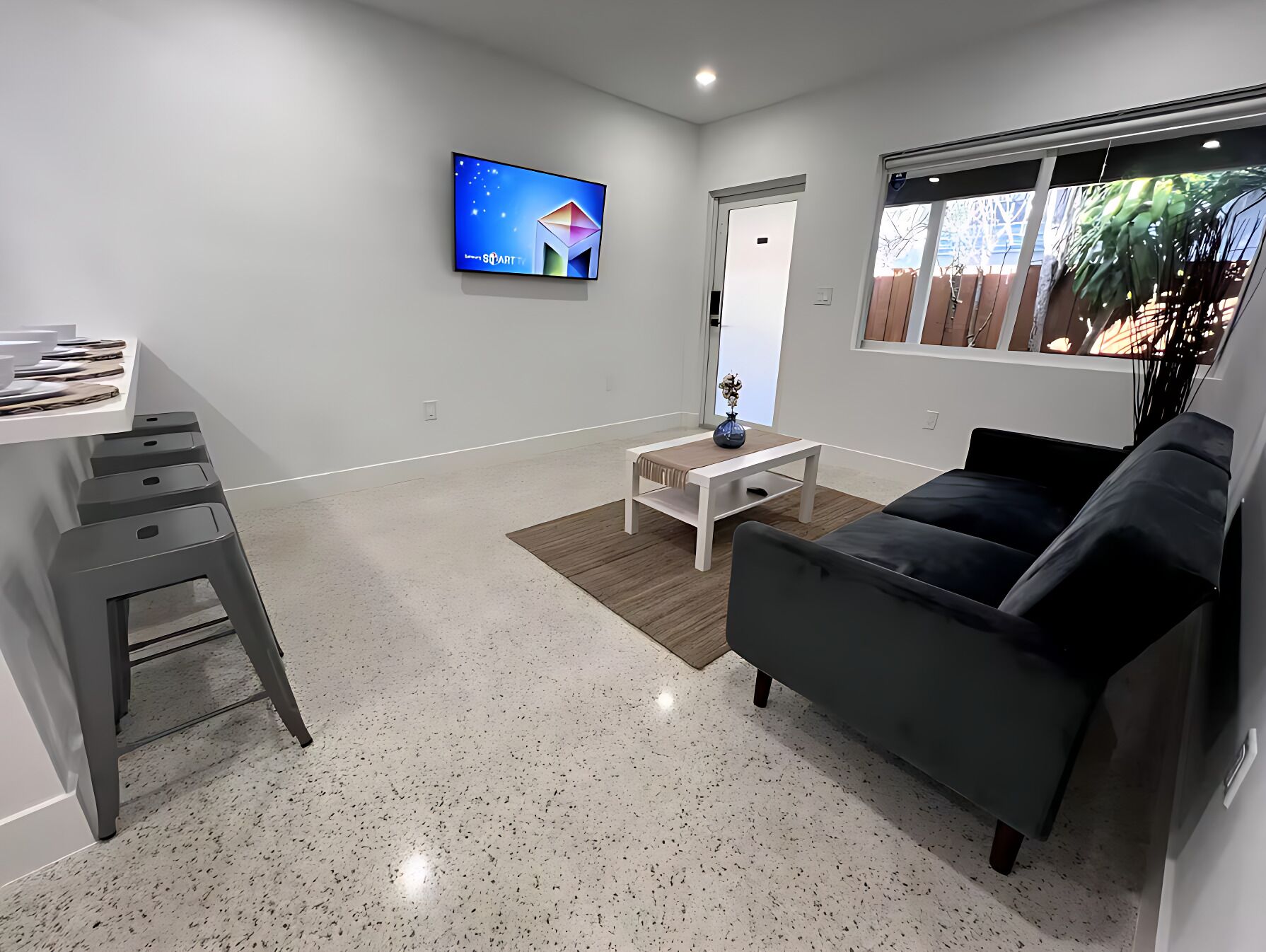 Una sala de estar moderna con un sofá gris, una mesa de centro blanca y un televisor montado en la pared.