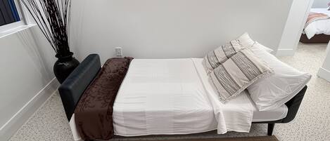 A bedroom with a bed, a bedside table, a lamp, and three framed pictures on the wall.
