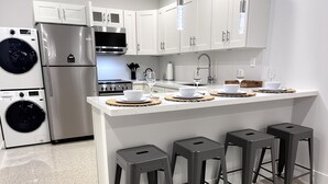 A modern kitchen with a central island, bar stools, a built-in washing machine, and a stainless steel refrigerator. - Casitas at Coconut Grove (Miami)