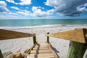 A wooden staircase leading to a sandy beach with a view of the ocean and a partly cloudy sky. - Manasota Beach House (Englewood)