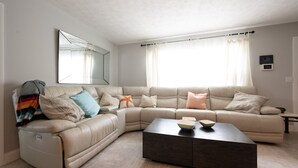 Una sala moderna con un sofá seccional beige, una mesa de centro de madera oscura y un espejo grande en la pared.
