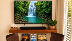 Een kamer met een televisie waarop een waterval te zien is, een Monopoly spelbord, boeken en een kaars op een tafel.
