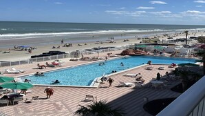 Un resort sulla spiaggia con piscina, sdraio, ombrelloni e vista sull'oceano.