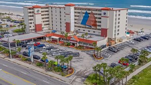 Un hotel a più piani con vista sulla spiaggia, parcheggio e un'imponente bandiera sull'edificio.
