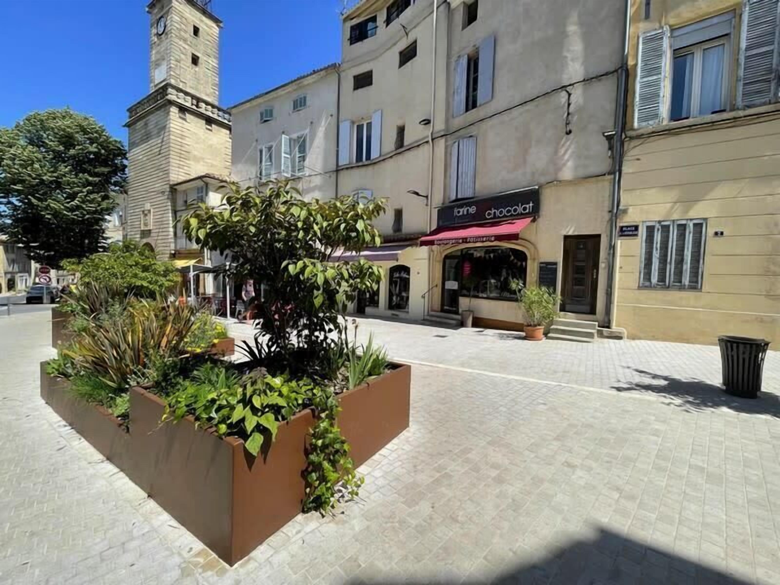 A square plaza with a central planter box containing various plants.