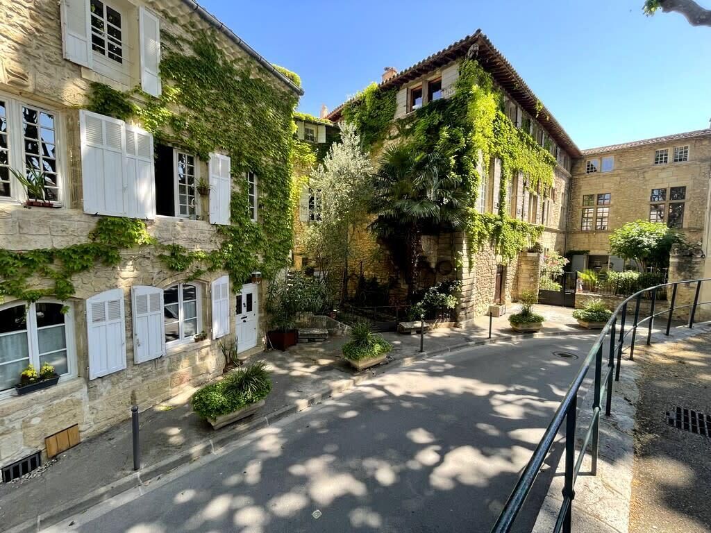 A narrow street with buildings on either side, some with shutters and greenery.