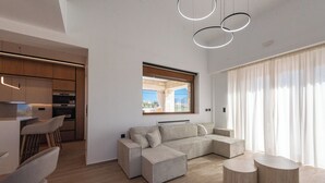 Una sala de estar moderna con un sofá seccional, un comedor con sillas, una cocina con armarios de madera y un ventanal con cortinas.